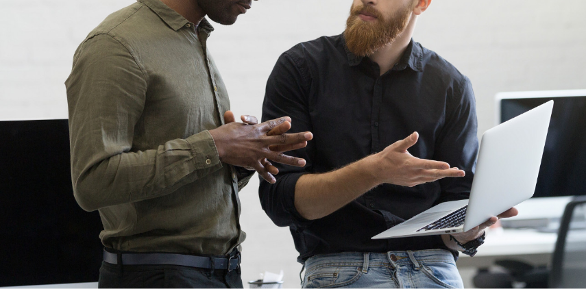 Error management - image of two men having a discussion while one holds and points to an open laptop
