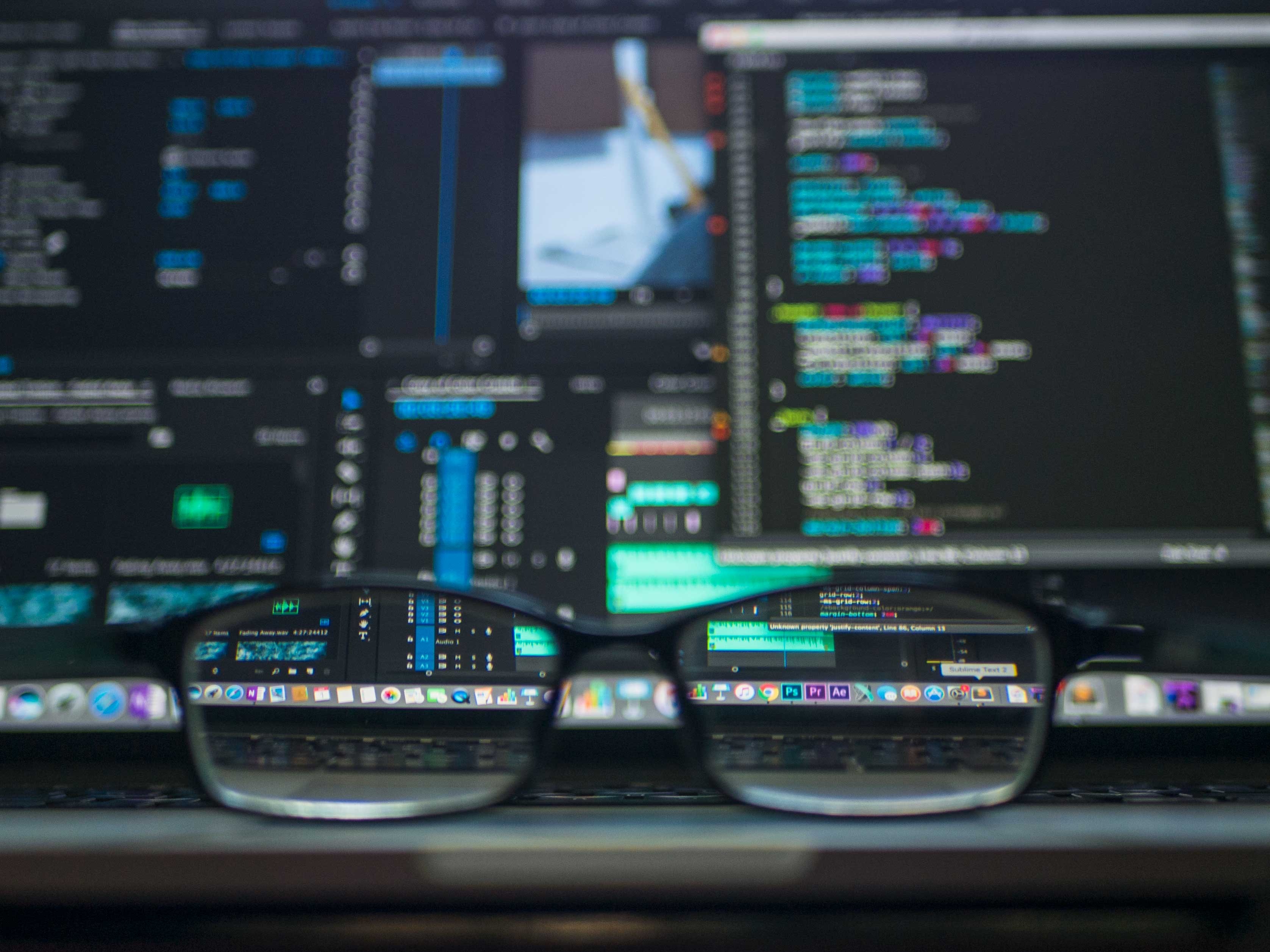 Image of eye glasses on a desk with computer screens in the background